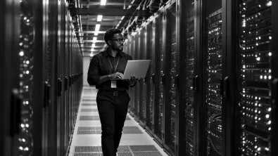An engineer carrying a laptop down a long data centre aisle between rows of server racks