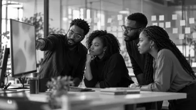A product team of four gathered at a monitor as one engineer points to the screen