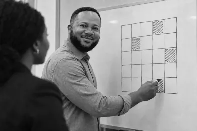 An engineer sketching a plan on a whiteboard while a colleague looks on